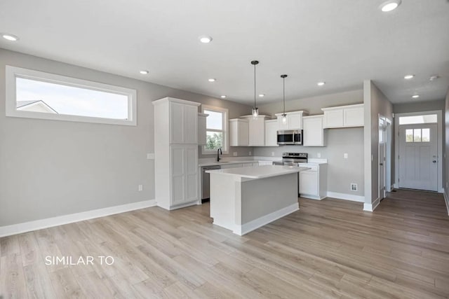 kitchen featuring decorative light fixtures, light wood-type flooring, a kitchen island, stainless steel appliances, and white cabinets