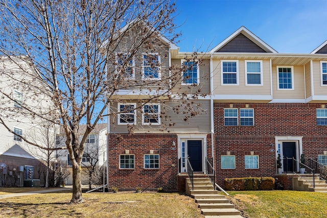 townhome / multi-family property featuring a front yard, central air condition unit, and brick siding