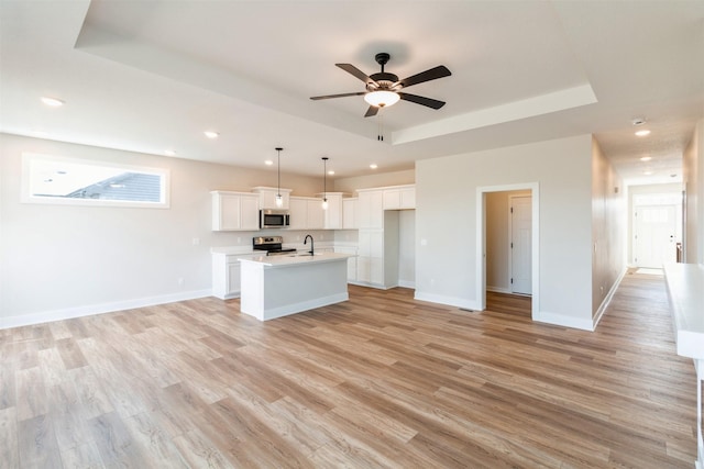 kitchen with appliances with stainless steel finishes, white cabinets, hanging light fixtures, a kitchen island with sink, and a tray ceiling