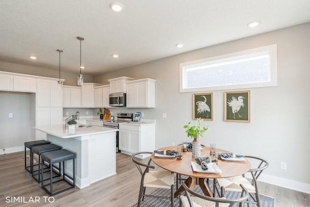 kitchen with sink, white cabinetry, stainless steel appliances, decorative light fixtures, and light wood-type flooring