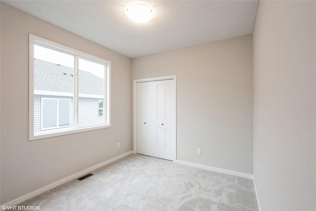 unfurnished bedroom featuring carpet floors, baseboards, visible vents, and a closet