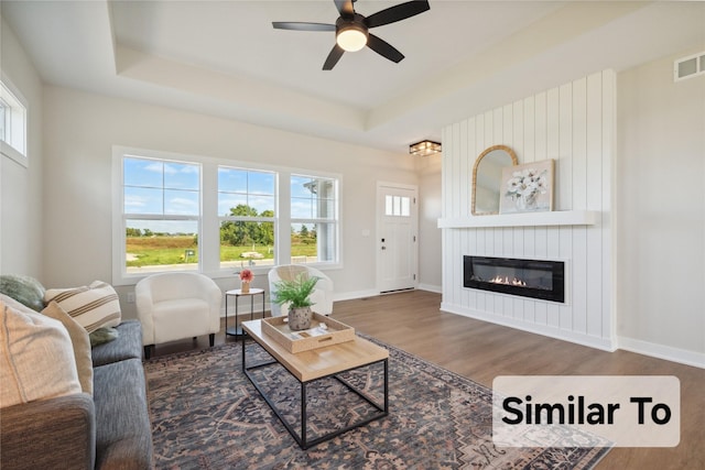 living room featuring a fireplace, a tray ceiling, a wealth of natural light, and dark hardwood / wood-style floors