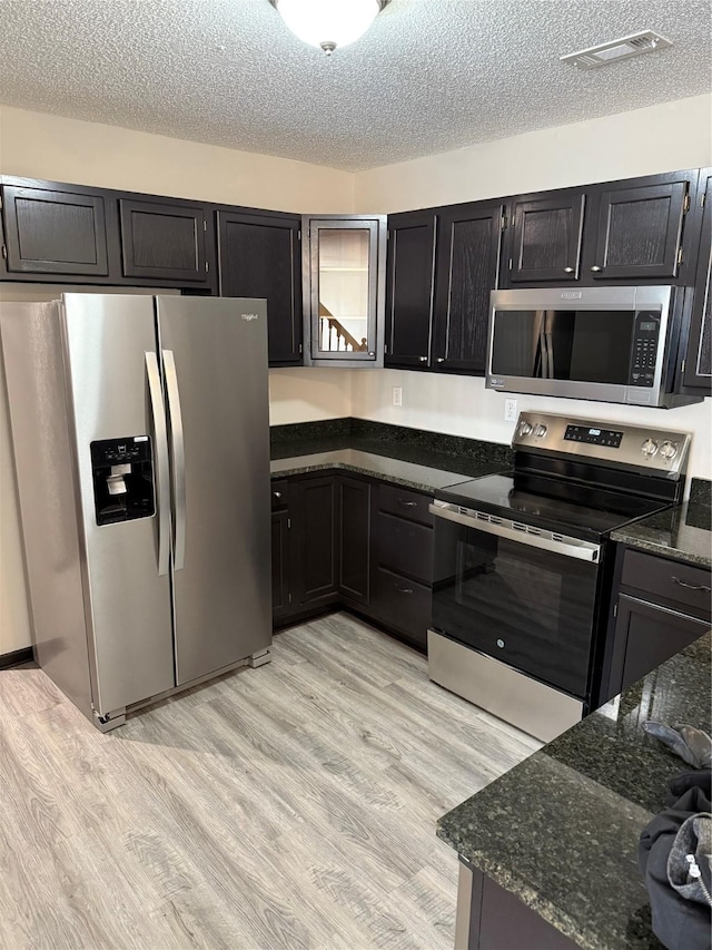 kitchen featuring appliances with stainless steel finishes, a textured ceiling, light wood-type flooring, and dark stone counters