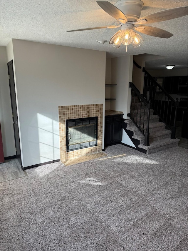 unfurnished living room featuring ceiling fan, carpet flooring, a fireplace, and a textured ceiling