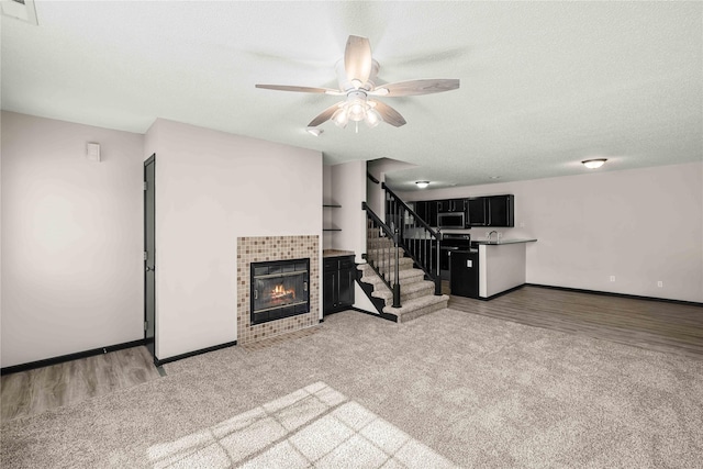 living room featuring visible vents, a tiled fireplace, a textured ceiling, baseboards, and stairs