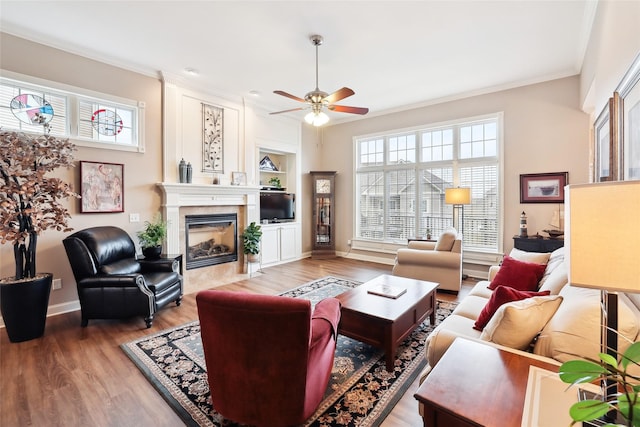 living area featuring built in features, a fireplace, light wood finished floors, ornamental molding, and baseboards