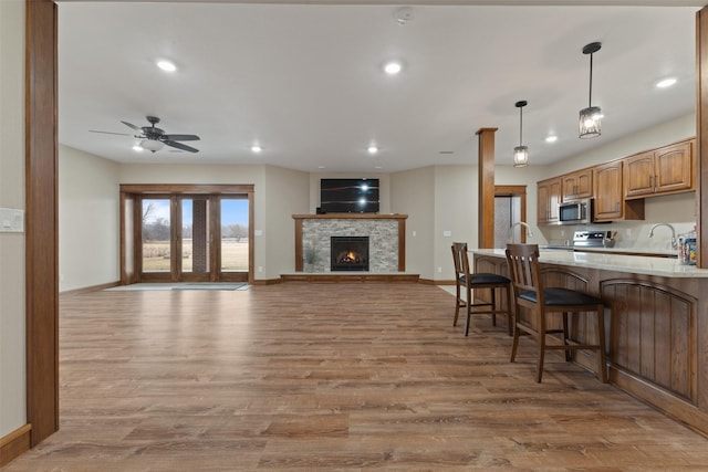 kitchen featuring a stone fireplace, a breakfast bar area, hanging light fixtures, light wood-type flooring, and stainless steel appliances