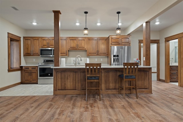 kitchen with decorative light fixtures, a center island with sink, light hardwood / wood-style floors, and appliances with stainless steel finishes