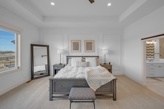 carpeted bedroom with sink, ensuite bath, and a tray ceiling