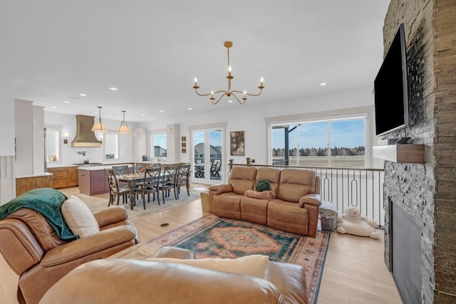 living room featuring a stone fireplace, a chandelier, and light hardwood / wood-style flooring