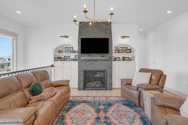 living room featuring a stone fireplace, a chandelier, built in features, and light hardwood / wood-style floors