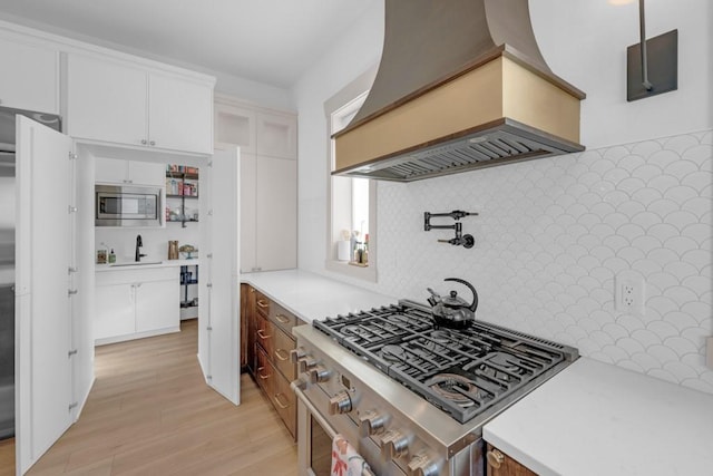 kitchen featuring white cabinetry, backsplash, custom exhaust hood, stainless steel appliances, and light wood-type flooring