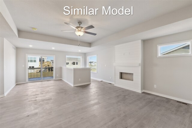 unfurnished living room featuring hardwood / wood-style floors, a tray ceiling, a large fireplace, and ceiling fan