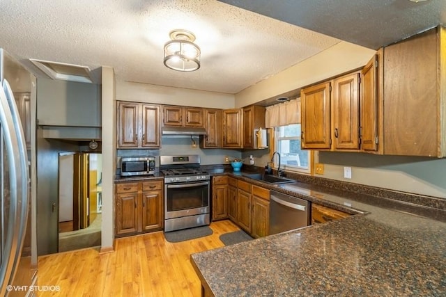 kitchen featuring appliances with stainless steel finishes, sink, light wood-type flooring, dark stone counters, and a textured ceiling