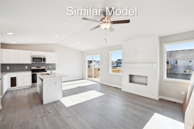 kitchen with white cabinetry, backsplash, stainless steel appliances, a center island with sink, and vaulted ceiling