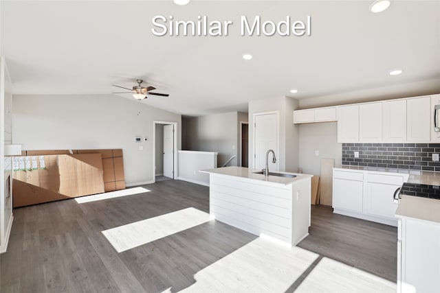 kitchen with vaulted ceiling, an island with sink, a sink, and white cabinetry