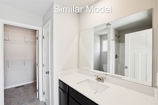 bathroom with visible vents, toilet, walk in shower, a walk in closet, and vanity