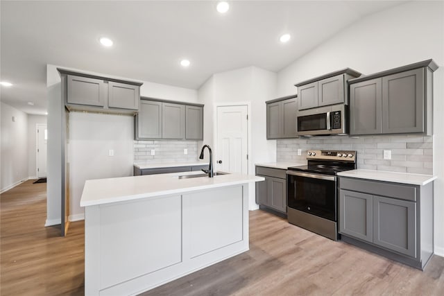 3423 5th Ave SE, Altoona, IA 50009 - kitchen featuring appliances with stainless steel finishes, gray cabinetry, an island with sink, tasteful backsplash, and light wood finished floors