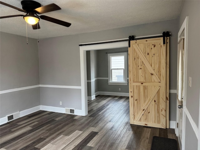 unfurnished room featuring ceiling fan, dark wood-type flooring, a barn door, and a textured ceiling