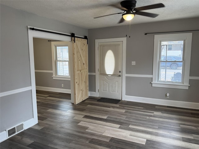 foyer entrance featuring ceiling fan, dark wood-type flooring, a barn door, and a textured ceiling