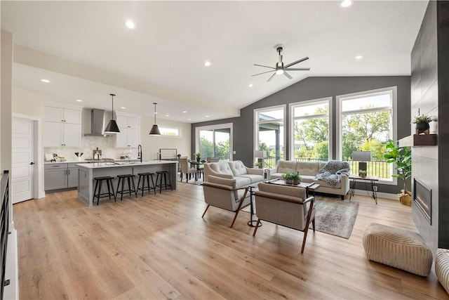 living room with vaulted ceiling, light wood-type flooring, sink, and a fireplace