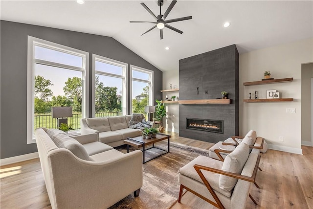 living room with vaulted ceiling, ceiling fan, a fireplace, and light hardwood / wood-style floors