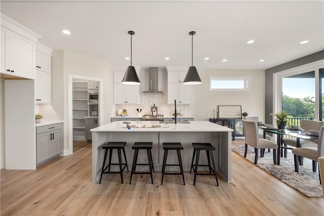 kitchen with pendant lighting, an island with sink, sink, white cabinets, and wall chimney exhaust hood