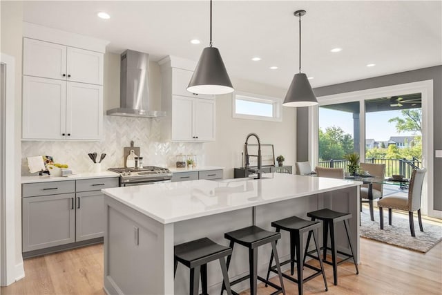 kitchen with pendant lighting, wall chimney range hood, sink, and an island with sink