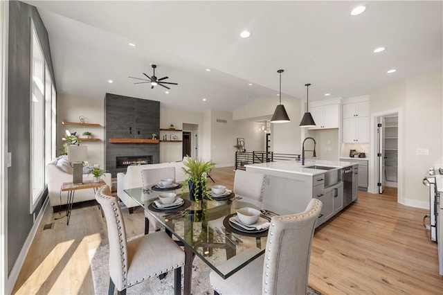 dining area featuring vaulted ceiling, a fireplace, light hardwood / wood-style floors, and sink