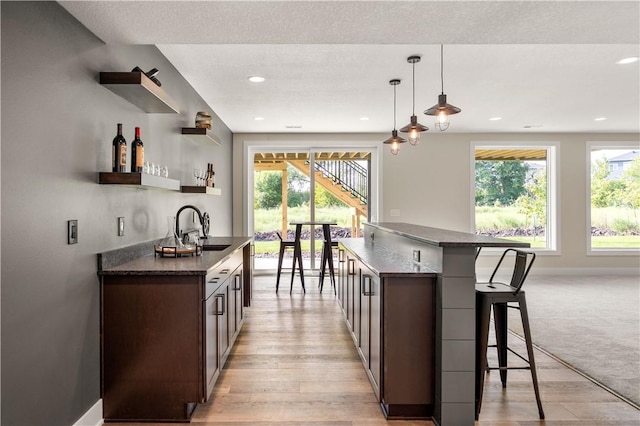 kitchen featuring sink, dark stone countertops, dark brown cabinets, a kitchen breakfast bar, and decorative light fixtures