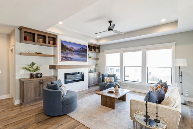 living room with hardwood / wood-style floors, a tray ceiling, and ceiling fan