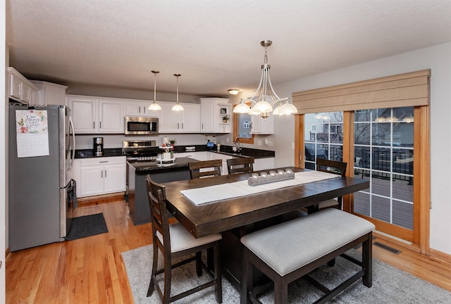 dining space featuring a textured ceiling, a notable chandelier, and light wood-type flooring