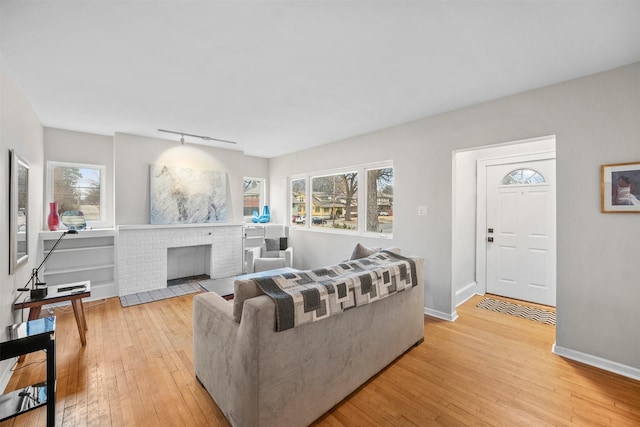 living room featuring track lighting, plenty of natural light, a brick fireplace, and light hardwood / wood-style flooring