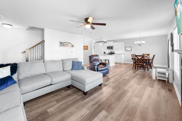 living room featuring ceiling fan with notable chandelier and light hardwood / wood-style flooring