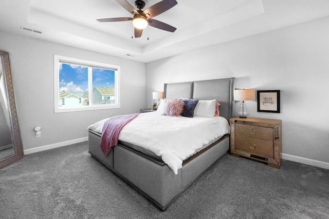 bedroom featuring dark carpet, a tray ceiling, and ceiling fan