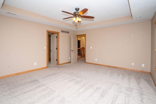 empty room featuring a raised ceiling, ceiling fan, light colored carpet, and a textured ceiling