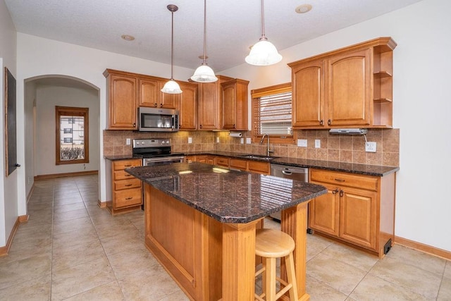 kitchen with sink, a center island, hanging light fixtures, appliances with stainless steel finishes, and decorative backsplash