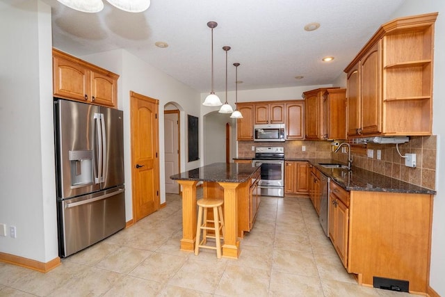 kitchen featuring sink, stainless steel appliances, a center island, a kitchen bar, and dark stone counters