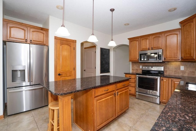 kitchen with tasteful backsplash, light tile patterned floors, a kitchen island, pendant lighting, and stainless steel appliances