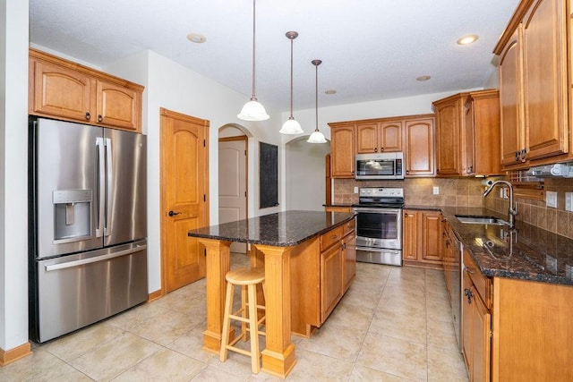 kitchen with appliances with stainless steel finishes, sink, dark stone countertops, hanging light fixtures, and a center island