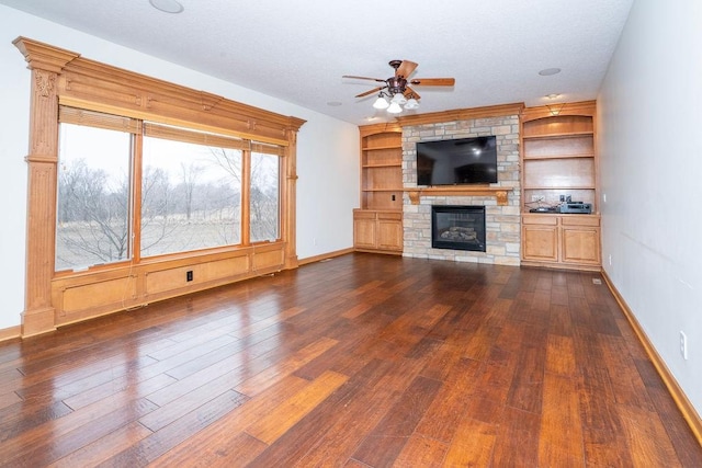 unfurnished living room featuring a large fireplace, built in features, dark hardwood / wood-style floors, and ceiling fan