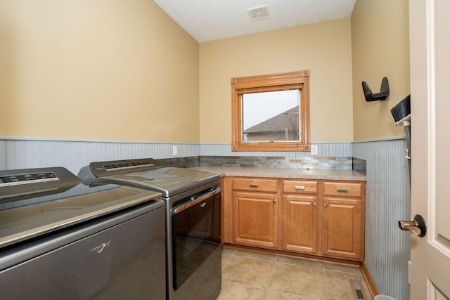 clothes washing area with separate washer and dryer, light tile patterned floors, and cabinets