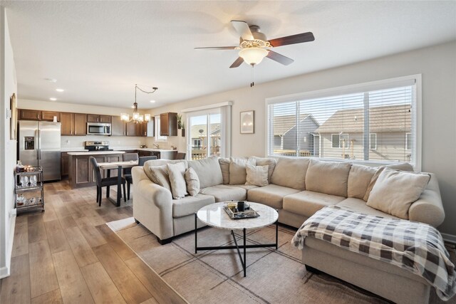 living room featuring ceiling fan with notable chandelier and light hardwood / wood-style floors