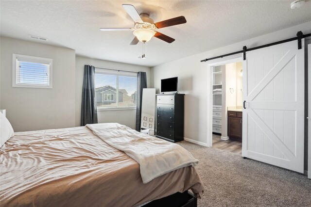 carpeted bedroom with ceiling fan, ensuite bath, a barn door, and a textured ceiling