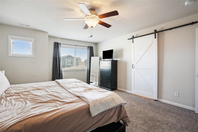 bedroom with ceiling fan, a barn door, a textured ceiling, and carpet flooring