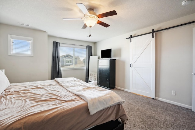 bedroom featuring a textured ceiling, a barn door, visible vents, baseboards, and carpet