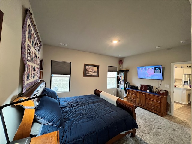 bedroom featuring stainless steel fridge with ice dispenser and light colored carpet