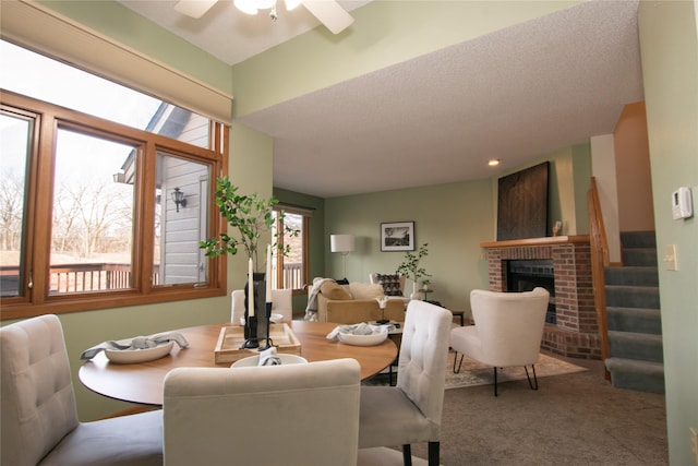 carpeted dining space featuring ceiling fan, a fireplace, and a textured ceiling