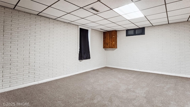 basement with a paneled ceiling, brick wall, and carpet floors