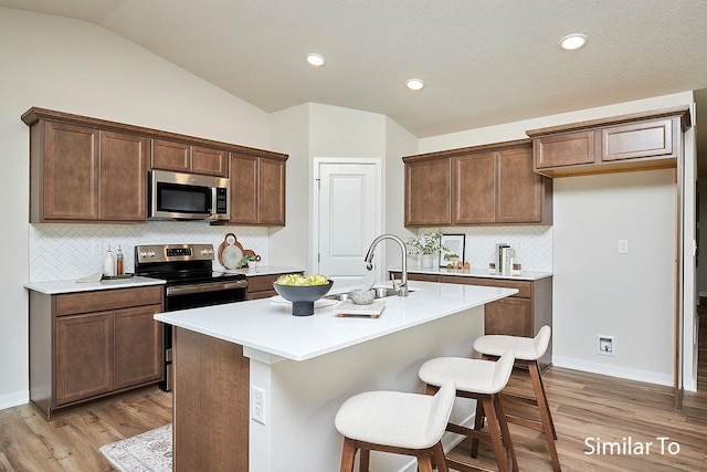 kitchen featuring sink, a breakfast bar, stainless steel appliances, a center island with sink, and vaulted ceiling